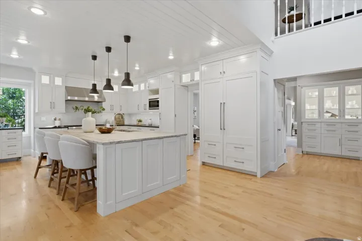 Gourmet kitchen featuring a large central island, white shaker cabinetry, hardwood flooring, integrated refrigeration, and a built-in microwave