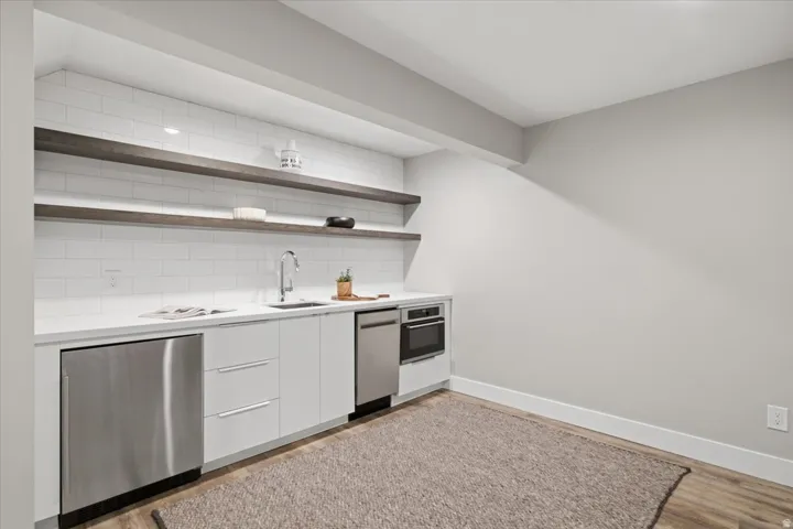 Full-size stainless steel refrigerator, white flat-panel cabinetry, integrated stainless steel dishwasher, built-in oven, and a white subway tile backsplash