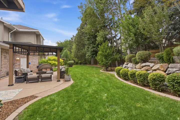 Expansive backyard featuring a stone retaining wall, mature trees, and a concrete patio with a built-in pergola