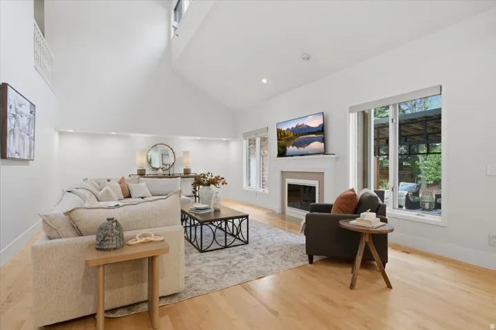 Vaulted ceilings, wood-finish flooring, a fireplace with a mantel, large windows, and recessed lighting