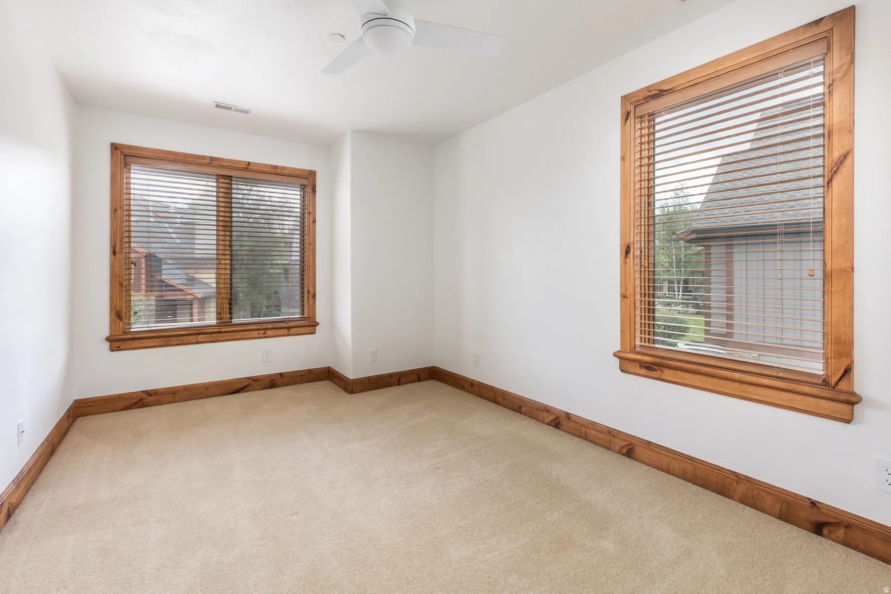 Bright corner room featuring two wood-trimmed windows with operable blinds, neutral carpet flooring, and wood-finish baseboard trim throughout