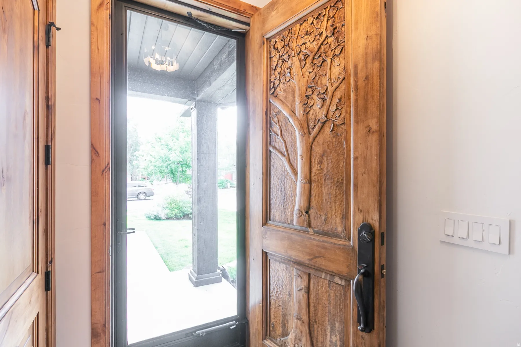 Carved wooden entry door with dark hardware, complemented by a glass storm door