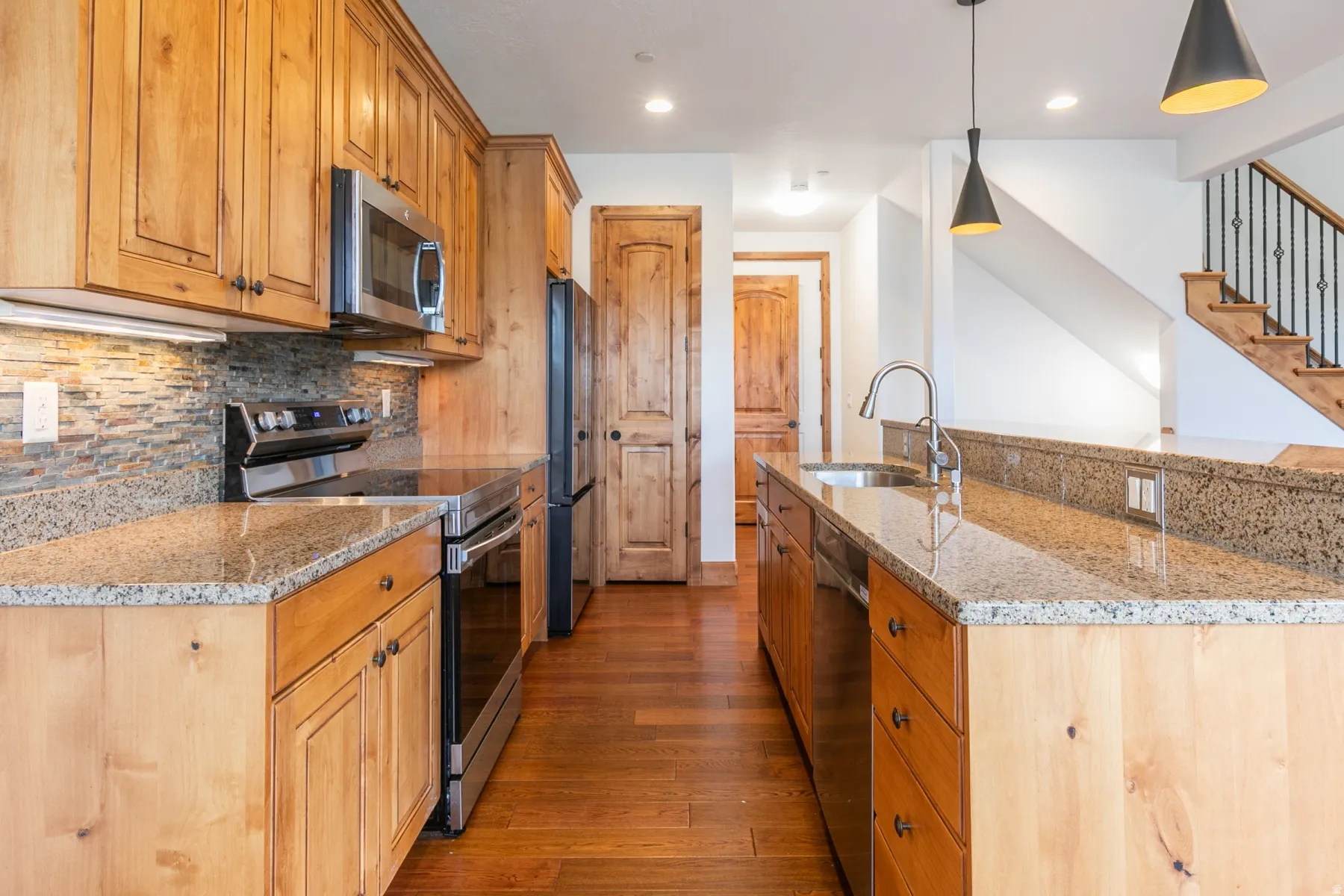 Chef's kitchen showcasing warm wood cabinetry, stainless steel appliances, granite countertops, and a mosaic tile backsplash