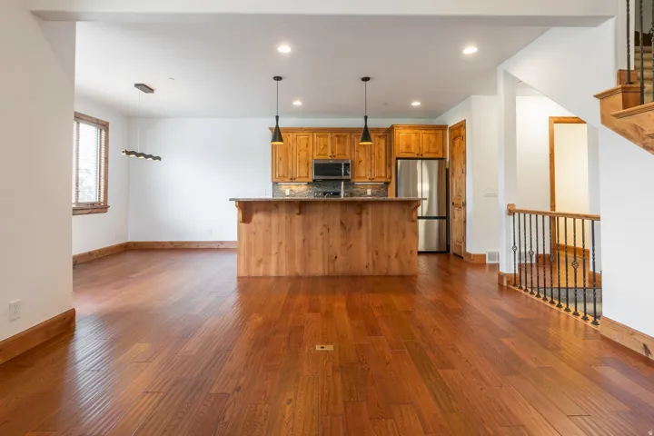 Hardwood flooring throughout, a kitchen island with stone countertop, wood cabinetry, recessed lighting, and a wood-finish staircase with decorative metal balusters