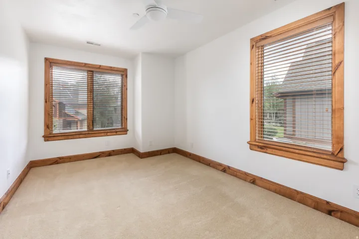 Bright corner room featuring two wood-trimmed windows with operable blinds, neutral carpet flooring, and wood-finish baseboard trim throughout
