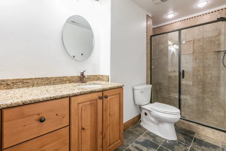 Granite-finish countertop vanity with a bronze-finish faucet, built-in cabinetry, and a walk-in shower with a glass enclosure