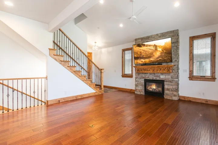 Spacious open-concept living area showcasing rich hardwood flooring, a stone fireplace with gas insert, and abundant natural light from multiple windows