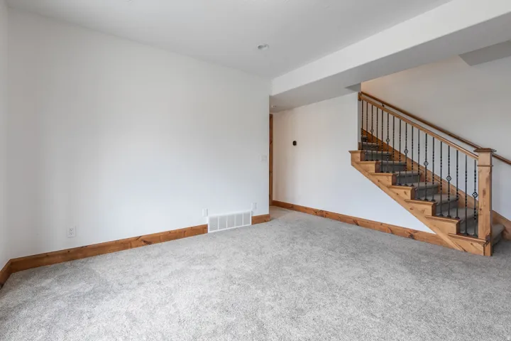 Spacious open living area featuring neutral carpet flooring, wood-trimmed architectural details, and a wooden staircase with metal railings