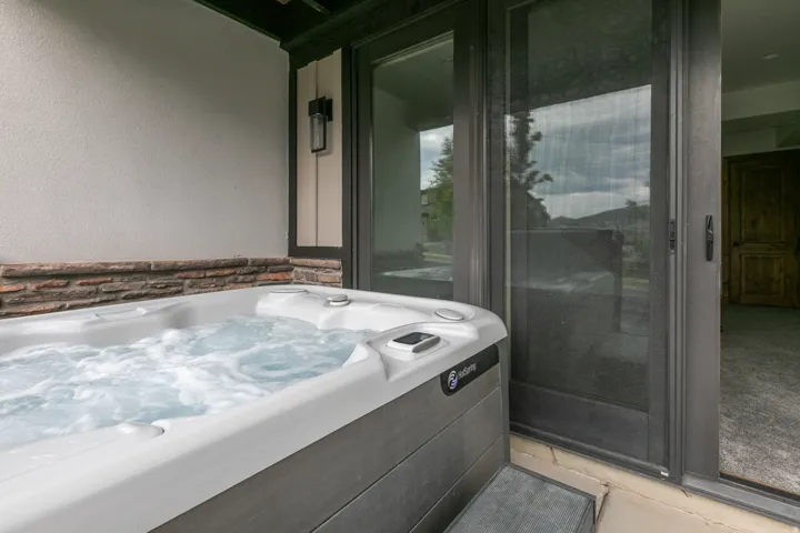 Built-in spa with bubbling water, textured exterior wall, stone accent trim, and a glass sliding door