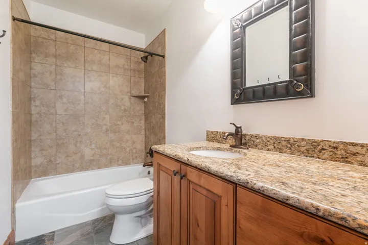 Spa-inspired bathroom featuring a wood-finish vanity with granite countertop, chrome faucet, and ample storage