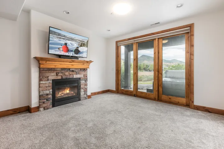 Spacious living room featuring a brick fireplace with gas insert and wood mantel, wall-mounted flat-screen television, large multi-panel sliding glass doors with wood framing, neutral carpet flooring, and recessed ceiling lighting