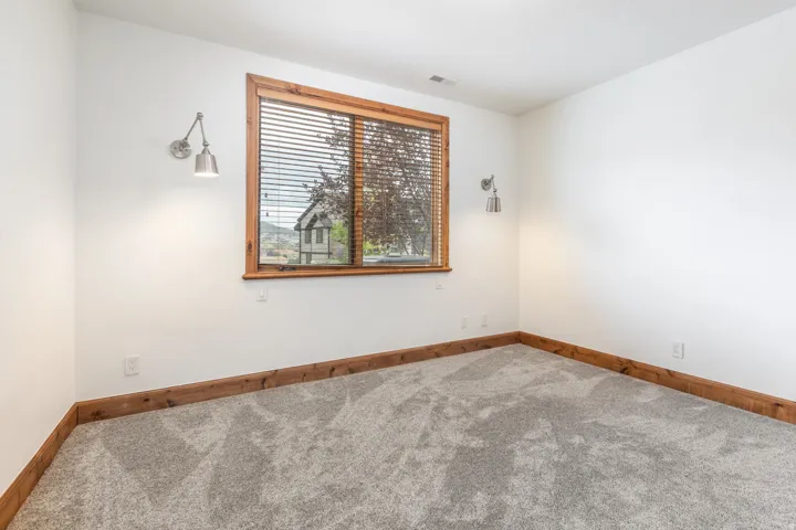 Bright corner bedroom with wood-trimmed window frame, carpeted flooring, and dual wall-mounted sconces providing ambient lighting