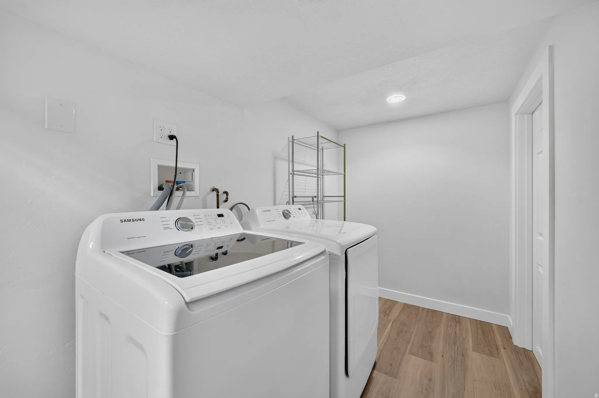 Modern laundry room featuring a front-load washer and dryer combination, white cabinetry with ample storage, polished countertop workspace, recessed lighting, and wood-finish flooring throughout