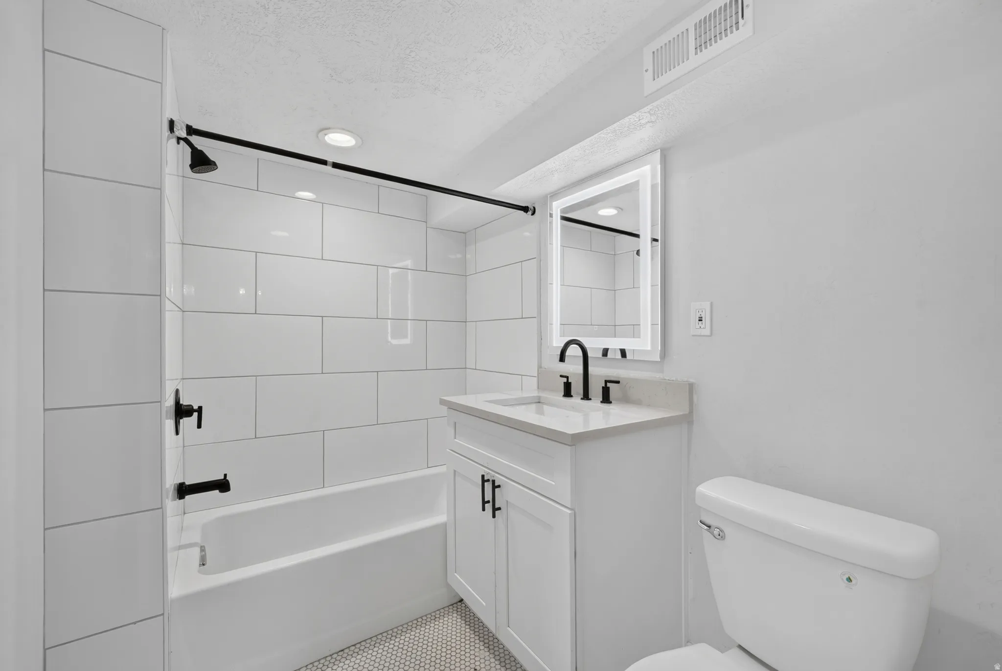 White subway tile shower surround, matte black fixtures, white vanity with stone countertop, round vessel sink, and illuminated mirror
