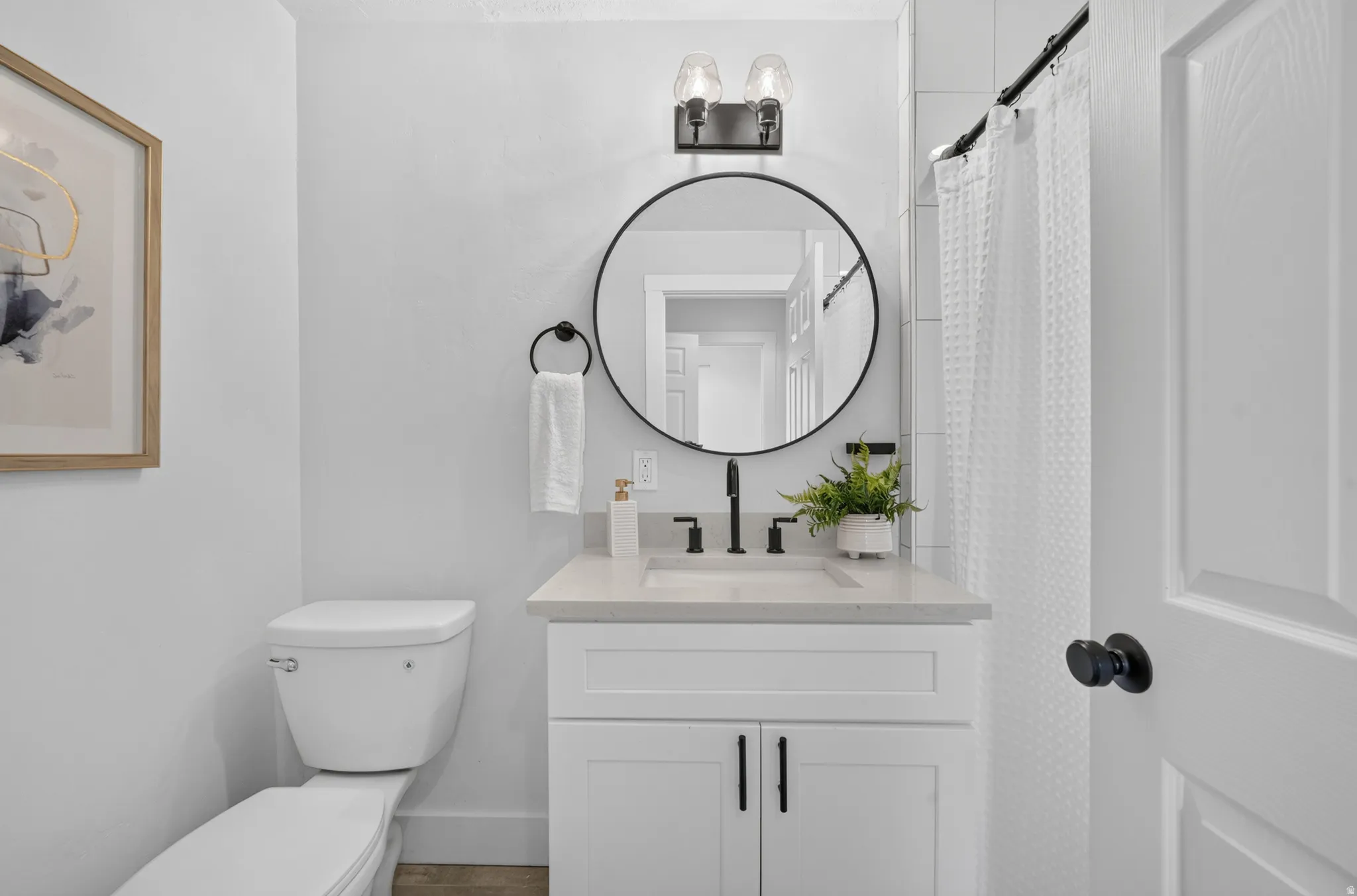 Modern bathroom featuring a white vanity with dual drawers and matte black hardware, quartz countertop, and a contemporary round mirror with black metal frame