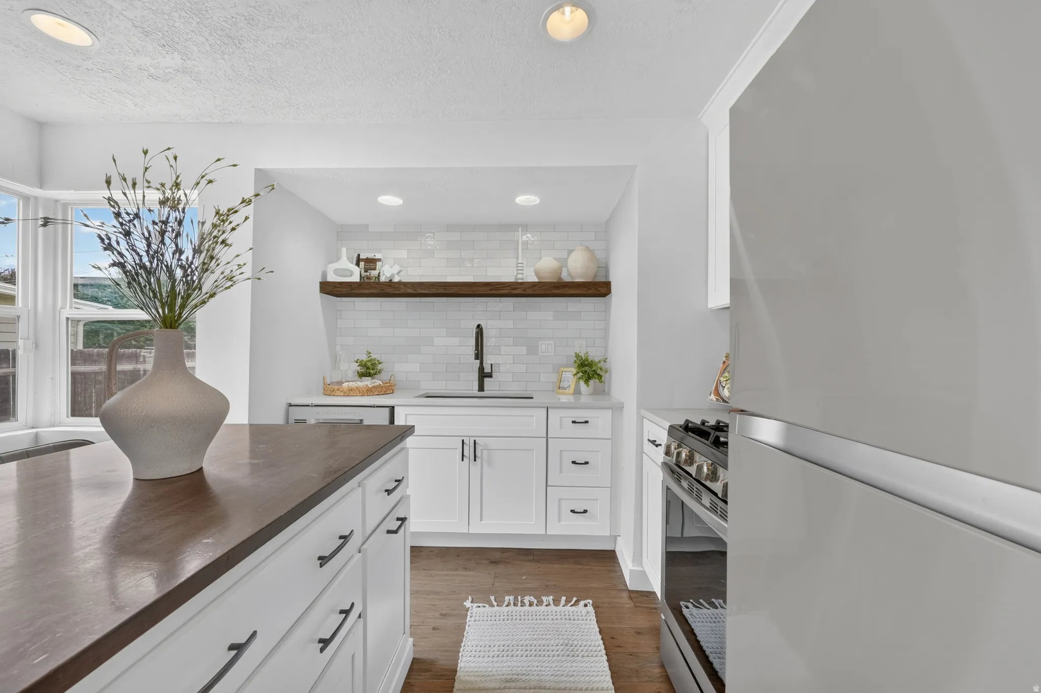 Modern kitchen featuring white cabinetry with integrated hardware, dark wood-finish countertops, stainless steel appliances including a professional-style range, subway tile backsplash, and recessed ceiling lighting