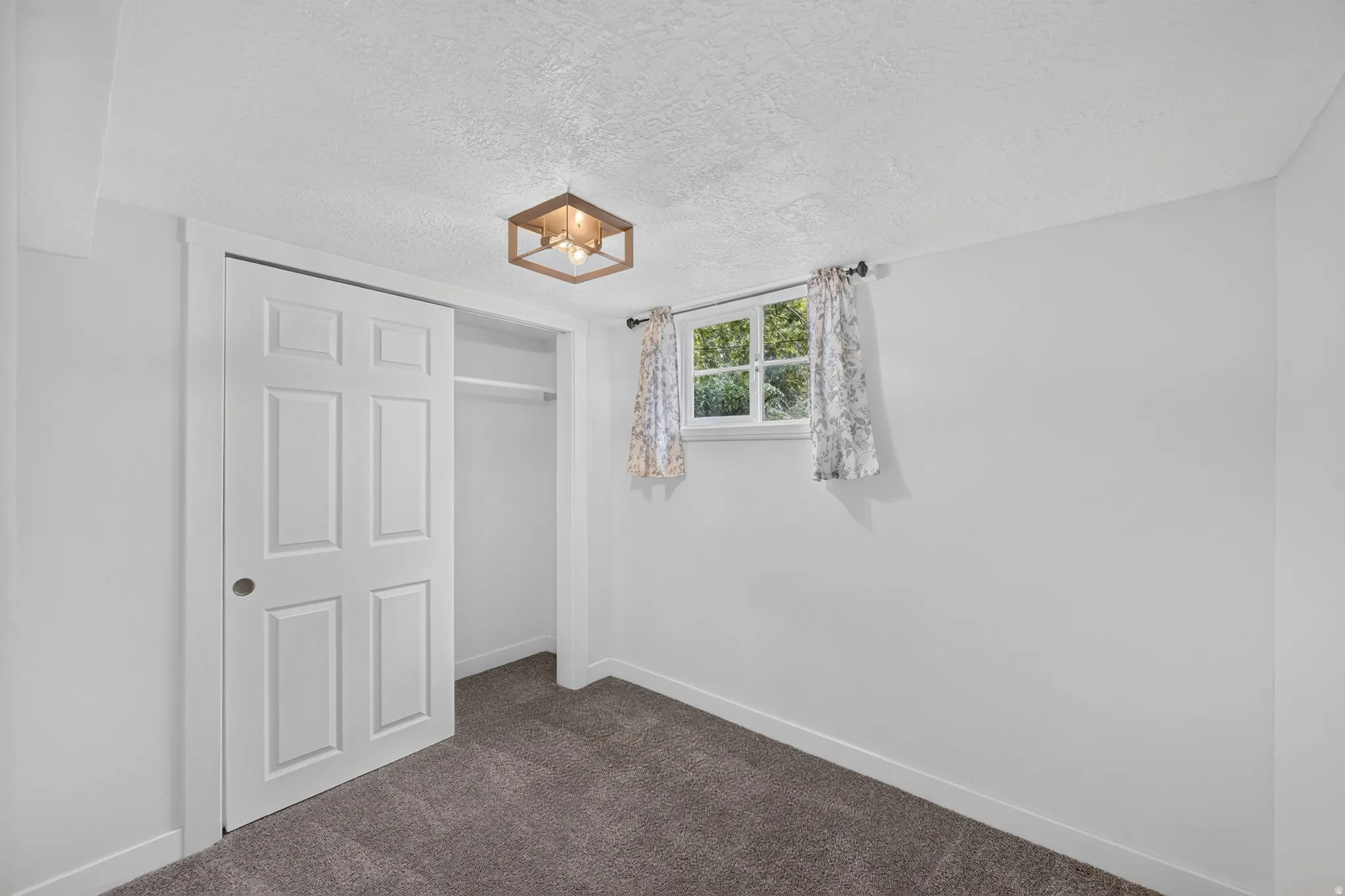 Bright bedroom with neutral wall finishes, dark carpet flooring, a six-panel closet door with shelving, and a window with natural light