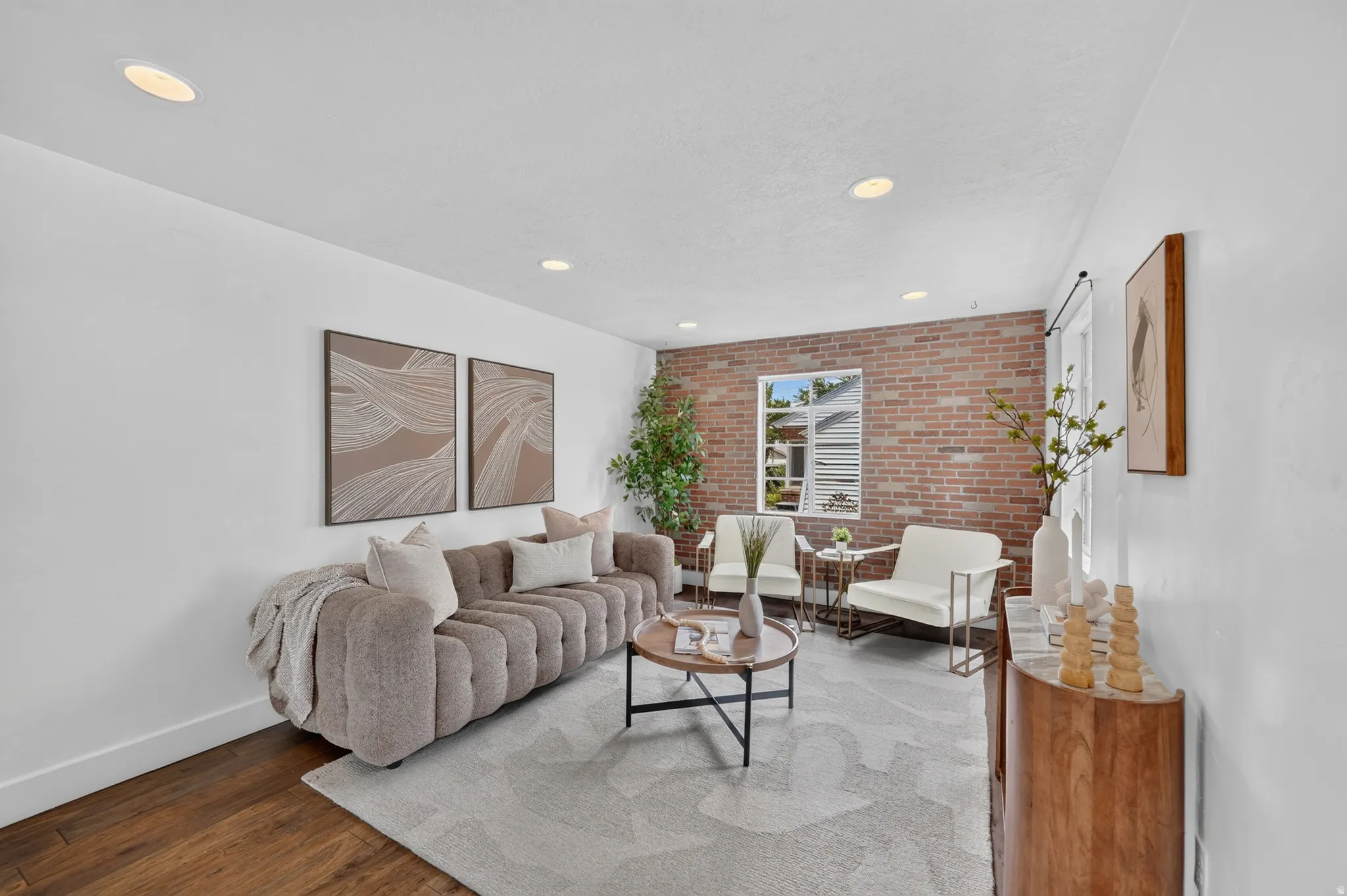 Sophisticated living room featuring exposed brick accent wall, recessed ceiling lighting, hardwood flooring, and a neutral color palette