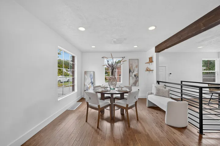 Open-concept dining area featuring hardwood flooring, recessed ceiling lighting, and a round dining table positioned beneath a large multi-pane window