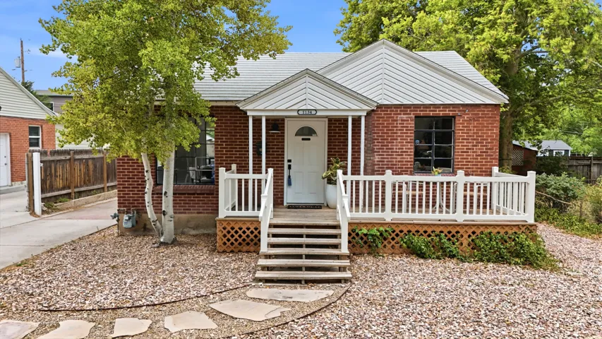 Charming brick home featuring a welcoming front porch with white railings and column supports, concrete steps, and a gabled roof with metal trim