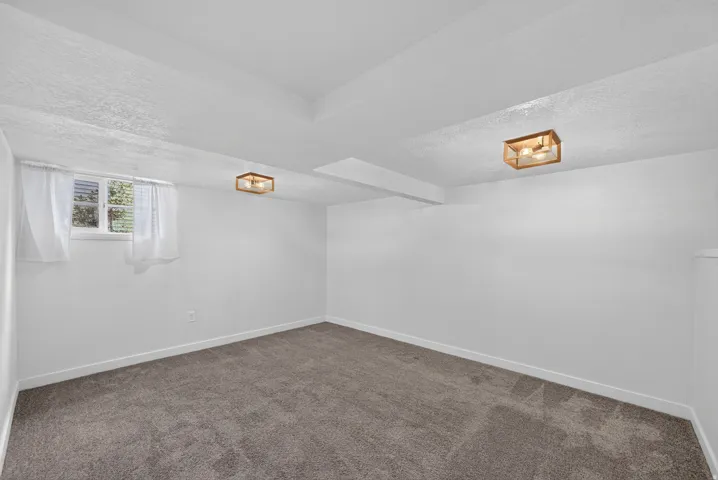 Finished basement room featuring neutral wall finishes, carpeted flooring, recessed ceiling details, and a small window with natural light