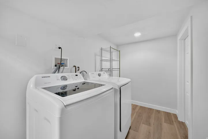 Modern laundry room featuring a front-load washer and dryer combination, white cabinetry with ample storage, polished countertop workspace, recessed lighting, and wood-finish flooring throughout
