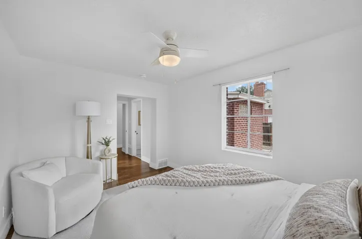 Bright, light-filled bedroom showcasing hardwood flooring, crisp white walls, and a ceiling fan with integrated lighting