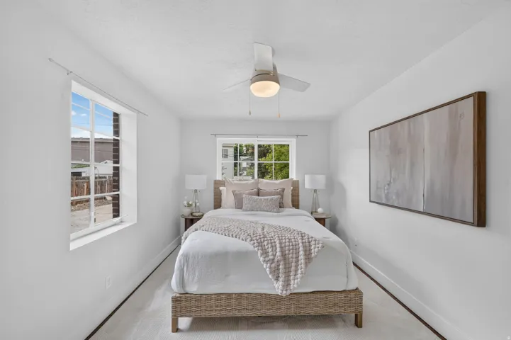 Bright secondary bedroom showcasing light wood-finish flooring, white walls, and recessed ceiling lighting with integrated fan