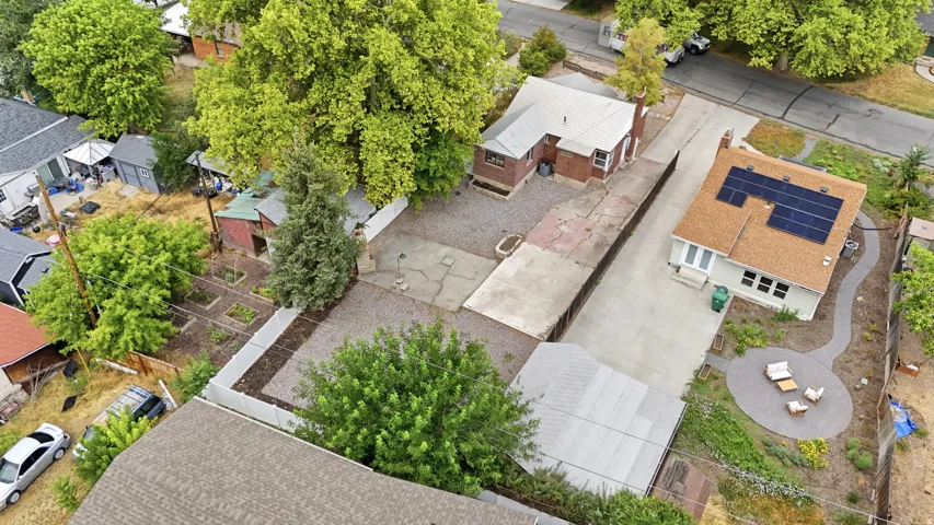 Aerial view showcasing a multi-structure property with mature landscaping, concrete hardscaping, and solar panel installation on the primary residence