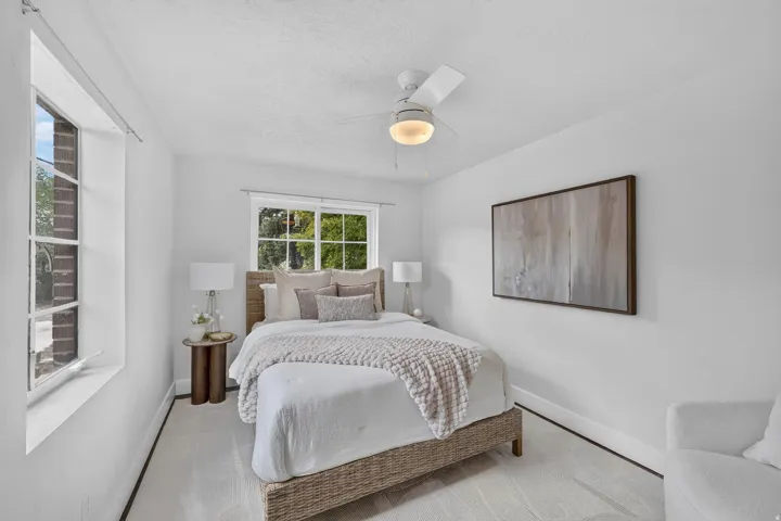 Bright bedroom featuring a wood-finish bed frame, soft white bedding, and woven throw blanket