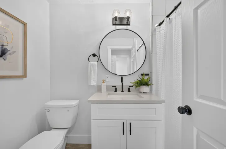Modern bathroom featuring a white vanity with dual drawers and matte black hardware, quartz countertop, and a contemporary round mirror with black metal frame