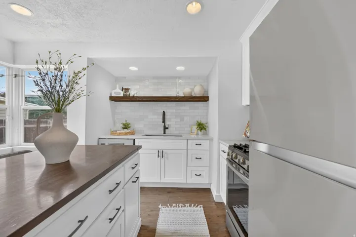 Modern kitchen featuring white cabinetry with integrated hardware, dark wood-finish countertops, stainless steel appliances including a professional-style range, subway tile backsplash, and recessed ceiling lighting