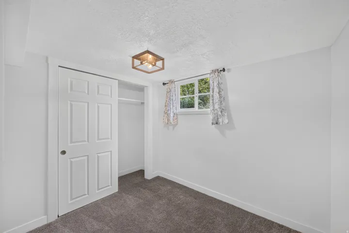 Bright bedroom with neutral wall finishes, dark carpet flooring, a six-panel closet door with shelving, and a window with natural light