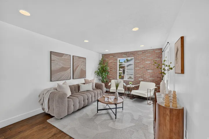 Sophisticated living room featuring exposed brick accent wall, recessed ceiling lighting, hardwood flooring, and a neutral color palette