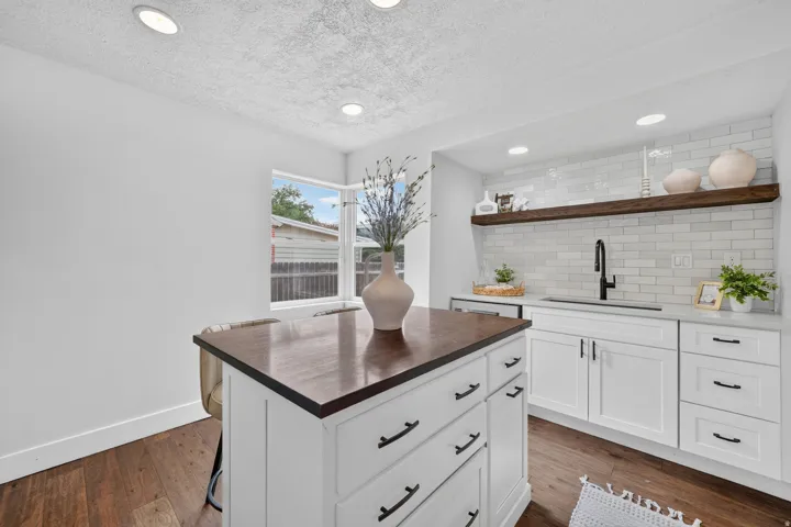 White cabinetry with matte black hardware, wood-finish flooring, white subway tile backsplash, recessed lighting, and a window