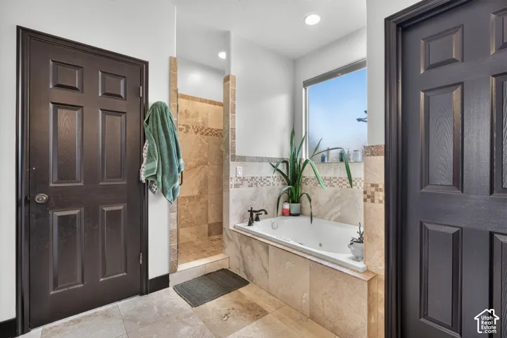 Spa-inspired primary bathroom featuring a soaking tub with tile surround, dual vanity with stone countertop and vessel sink, walk-in shower with glass enclosure, recessed lighting, and direct access to the bedroom
