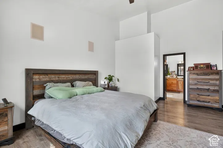 Spacious primary bedroom featuring a wood-frame bed with recessed headboard, warm wood-finish flooring, and abundant natural light