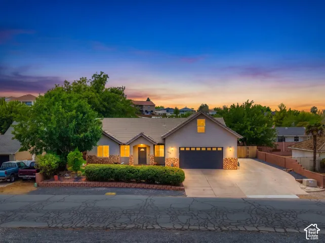 Charming single-story residence featuring a clean stucco exterior with stone accents, metal roof with multiple peaks, and an attached two-car garage with dark paneling