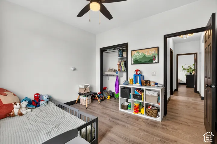 Bright bedroom with wood-finish flooring, ceiling fan with integrated lighting, and built-in shelving and storage cabinetry