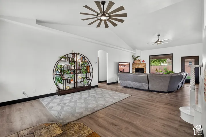 Spacious open-concept living area featuring wood-finish flooring, soaring ceilings with contemporary windmill-style ceiling fan, and abundant natural light