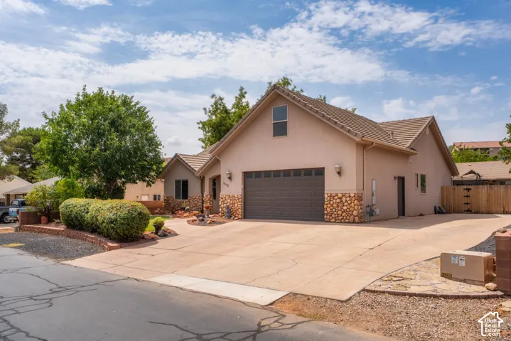 Stucco exterior with stone accents, a tile roof, an integrated two-car garage, an expansive concrete driveway, and mature landscaping