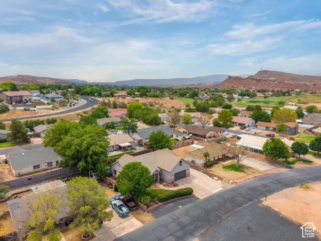 Aerial view showcasing this residential property situated on a generous lot with mature landscaping, established trees, and paved driveway