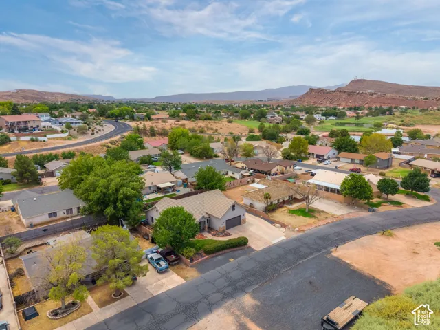 Aerial view showcasing this residential property situated on a corner lot with mature landscaping, paved driveway, and direct street access