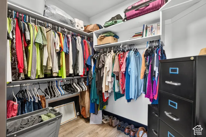Walk-in closet featuring extensive rod and rail organization, built-in shelving with upper storage for seasonal items, wood-finish flooring, and a black multi-drawer storage unit with chrome hardware for additional garment and accessory storage