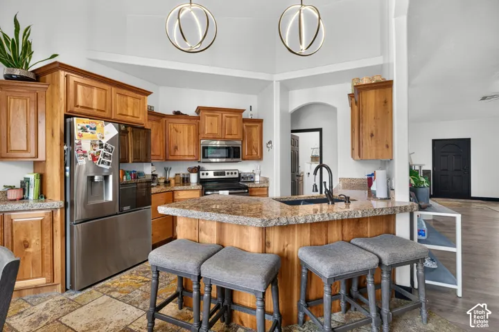 Chef's kitchen featuring warm wood cabinetry, stainless steel appliances including a gas range, granite countertops, a large center island with seating, pendant lighting, and stainless steel refrigerator with ice and water dispensers