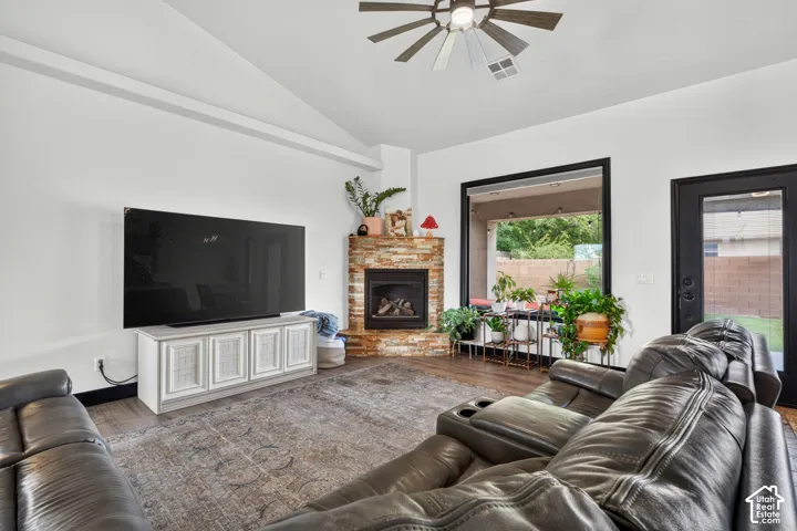 Spacious living room featuring a gas fireplace with brick surround and mantel, wall-mounted flat-screen television above white cabinetry, ceiling fan with brushed metal finish, plush leather seating, neutral area rug, and French doors opening to the backy