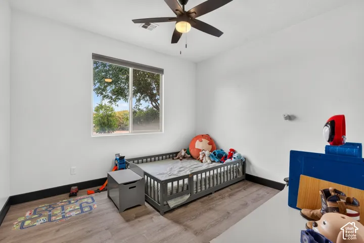Bright secondary bedroom featuring hard-surface wood-finish flooring, ceiling fan with integrated lighting, large window with natural light, and generous floor space suitable for multiple uses