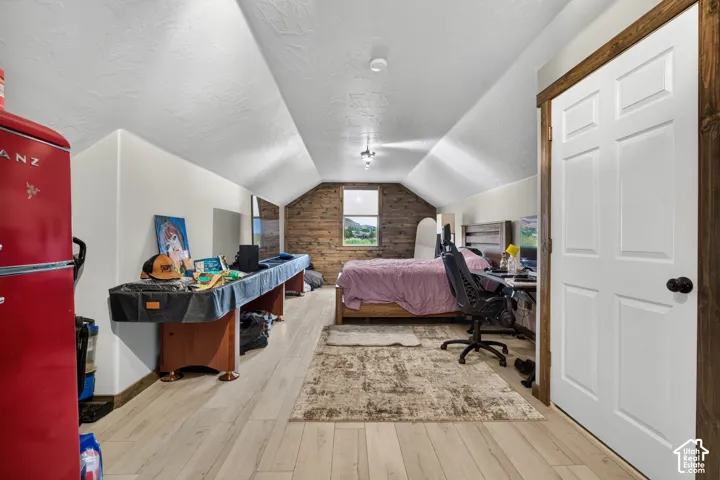 Versatile attic space featuring soaring vaulted ceilings with exposed wood beams, wood-finish flooring throughout, and abundant natural light from a brick chimney accent wall