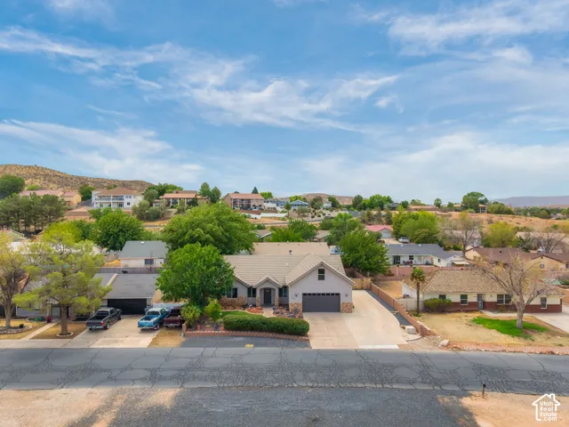 Aerial view showcasing a single-story residence with a neutral-toned stucco exterior, dark-finished roof, and circular driveway