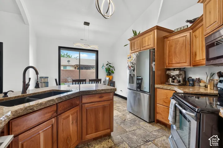 Spacious kitchen featuring warm wood cabinetry, stainless steel appliances, granite countertops, a large center island with undermount sink and gooseneck faucet, and abundant natural light from expansive windows overlooking the exterior